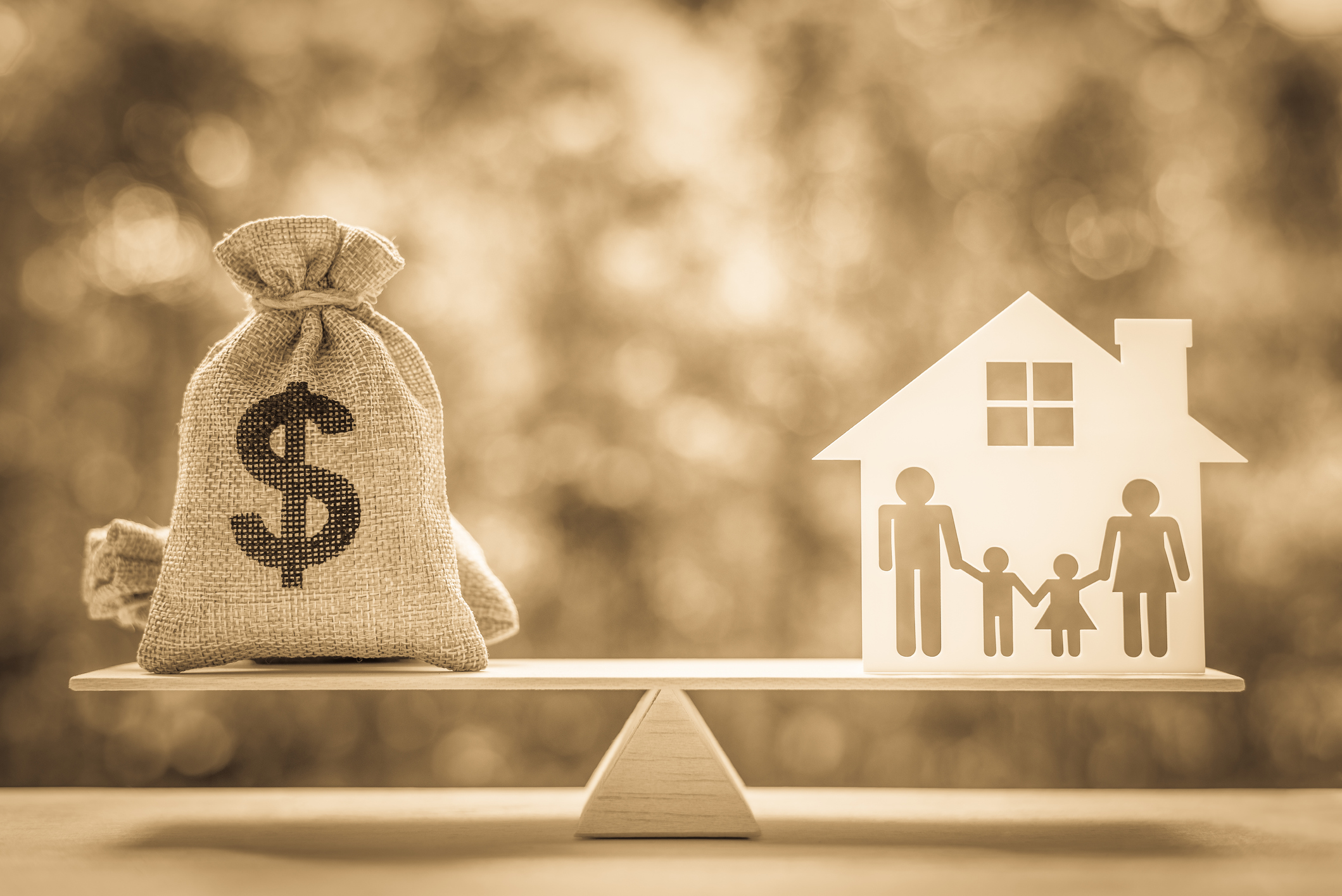 Photo of balance weighing bags of money against a family household.